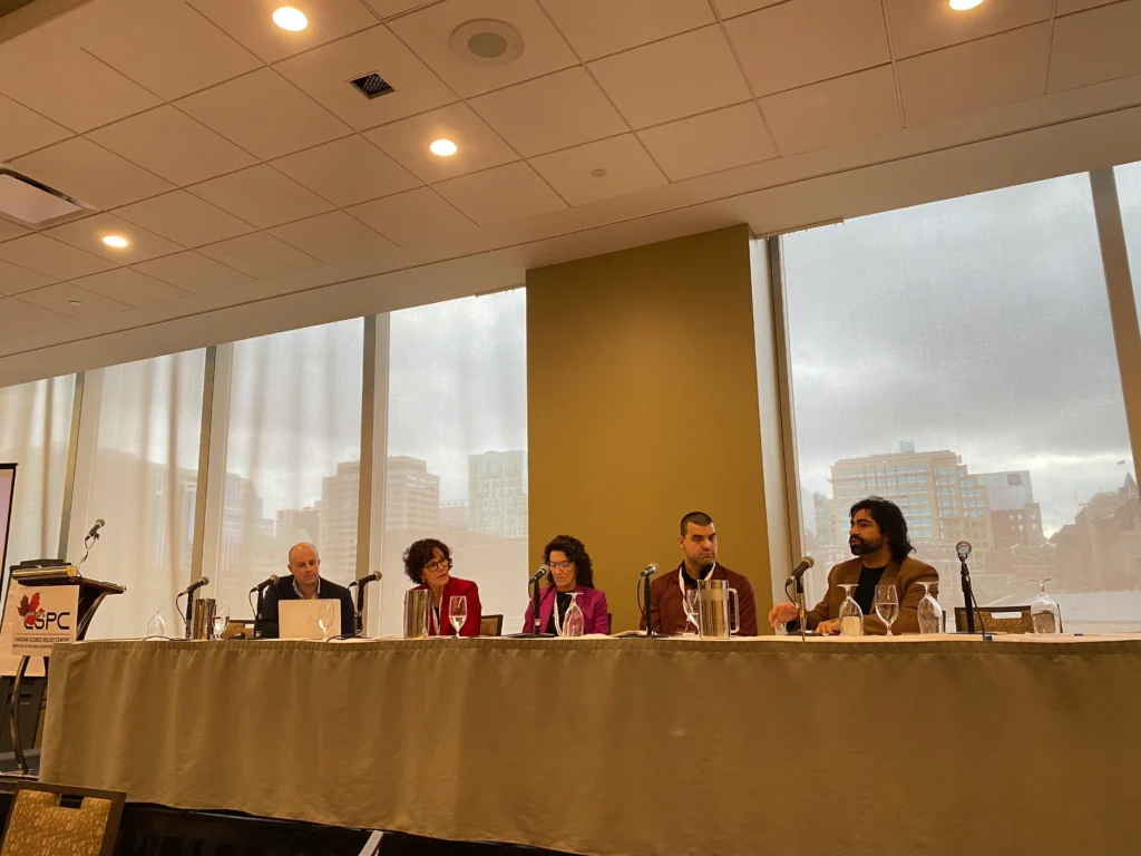 Photo of four panellists in front of a long table with a large window behind